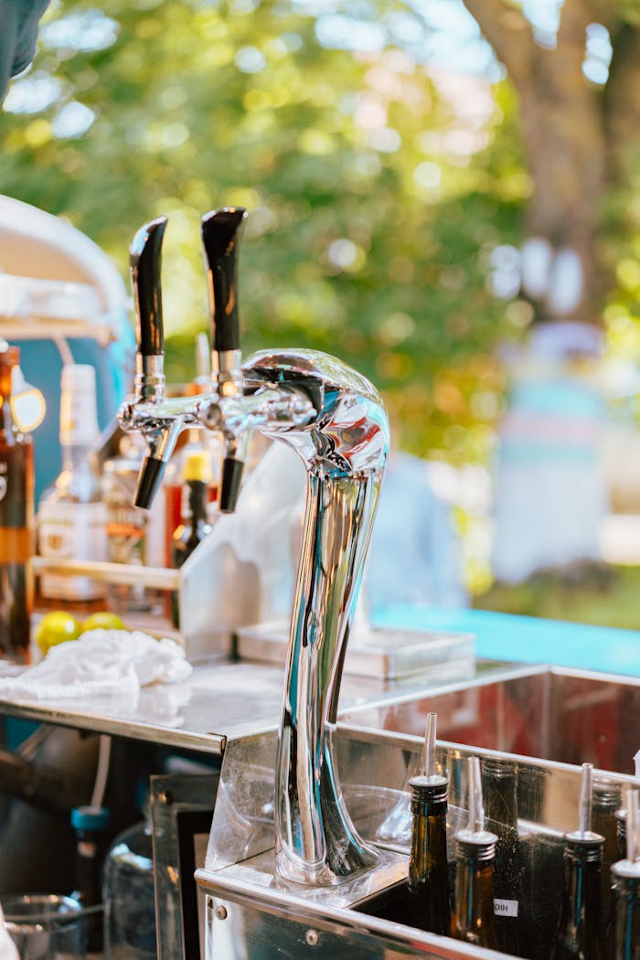 Close-up of shiny chrome beer taps at an outdoor bar setting during a sunny day.
